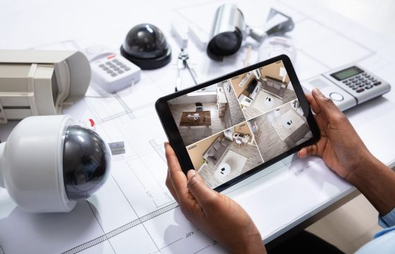 An Elevated View Of Person Watching Footage On Digital Tablet With Security Equipment On Blueprint