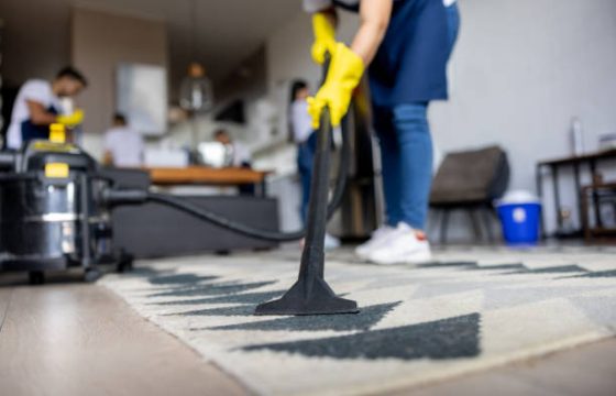 Close-up on a professional cleaner vacuuming a carpet while working at an apartment - housework concepts